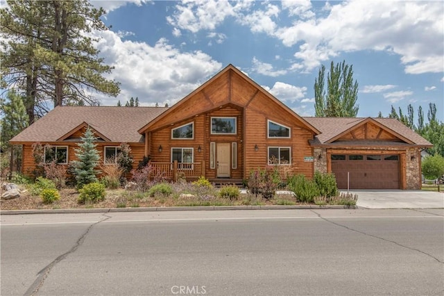 cabin with an attached garage, driveway, and roof with shingles