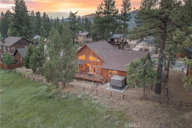 back of property at dusk featuring a shingled roof, a fenced backyard, and a wooden deck