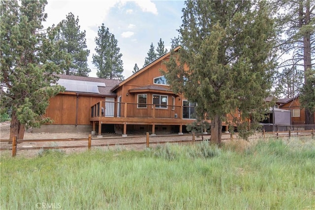 rear view of house with fence, a wooden deck, and roof mounted solar panels