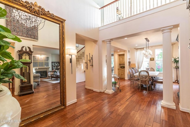 foyer entrance featuring wood-type flooring, a towering ceiling, decorative columns, and a notable chandelier