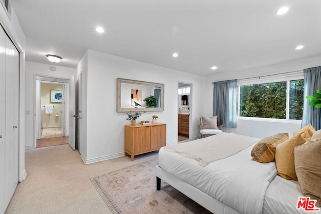 bedroom with ensuite bathroom, light carpet, and a closet