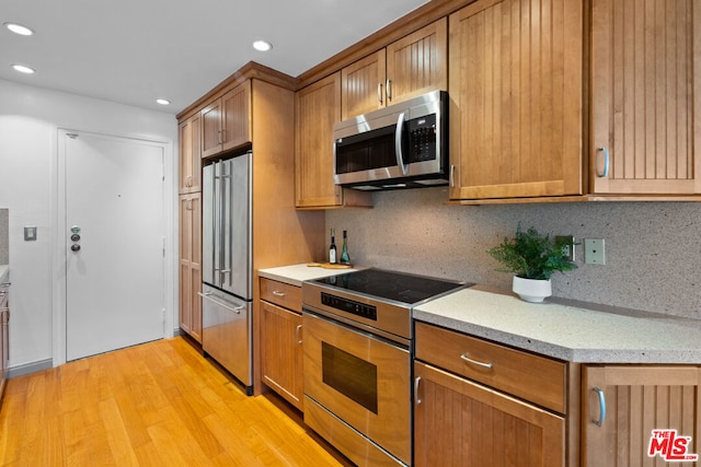 kitchen with decorative backsplash, stainless steel appliances, light hardwood / wood-style flooring, and light stone counters