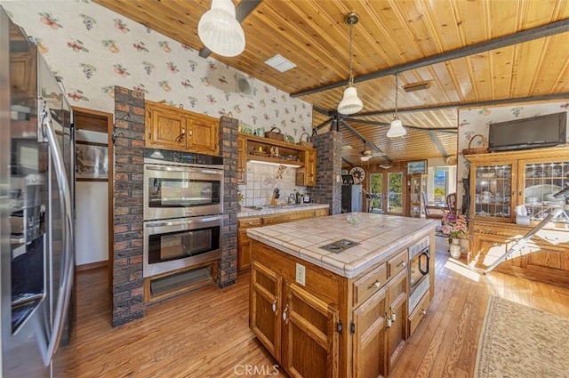 kitchen featuring appliances with stainless steel finishes, decorative light fixtures, light hardwood / wood-style floors, tile counters, and lofted ceiling