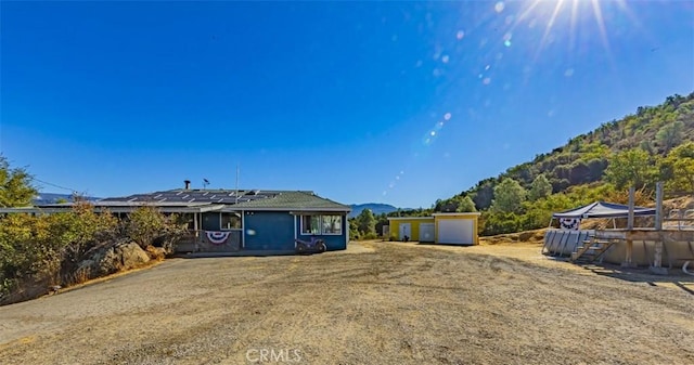 rear view of property with a mountain view, a garage, an outdoor structure, and solar panels