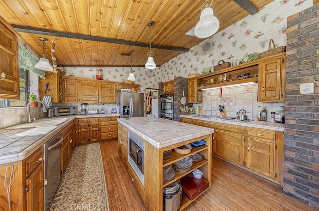 kitchen featuring tile countertops, stainless steel appliances, hanging light fixtures, and light hardwood / wood-style flooring