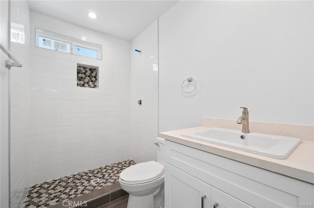 bathroom with a tile shower, vanity, and toilet