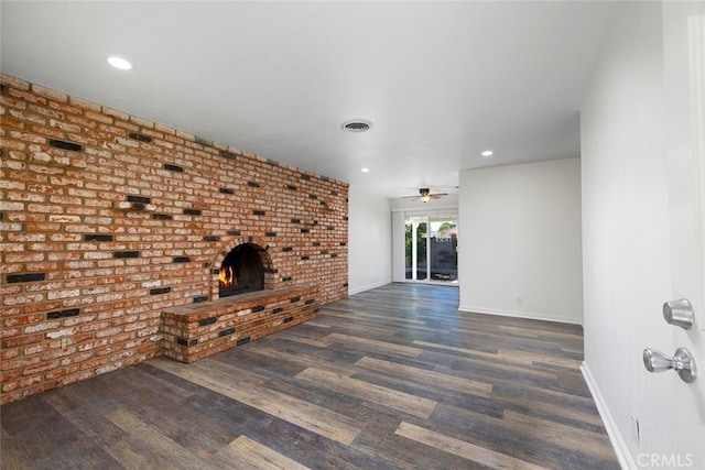 unfurnished living room featuring ceiling fan, a fireplace, dark wood-type flooring, and brick wall