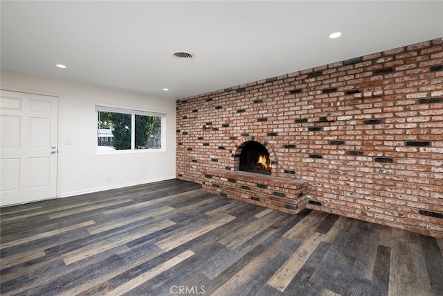 unfurnished living room featuring dark hardwood / wood-style flooring, brick wall, and a brick fireplace