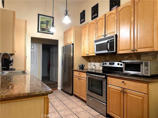 kitchen featuring stainless steel appliances, sink, pendant lighting, light tile patterned floors, and dark stone countertops