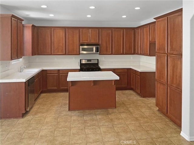 kitchen featuring stainless steel appliances, a sink, a kitchen island, tile counters, and brown cabinets