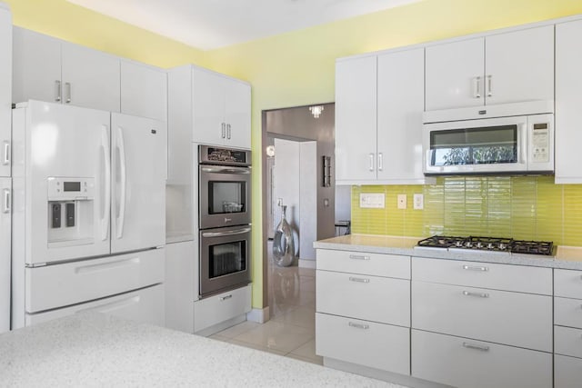 kitchen featuring light tile patterned floors, white cabinetry, backsplash, and appliances with stainless steel finishes