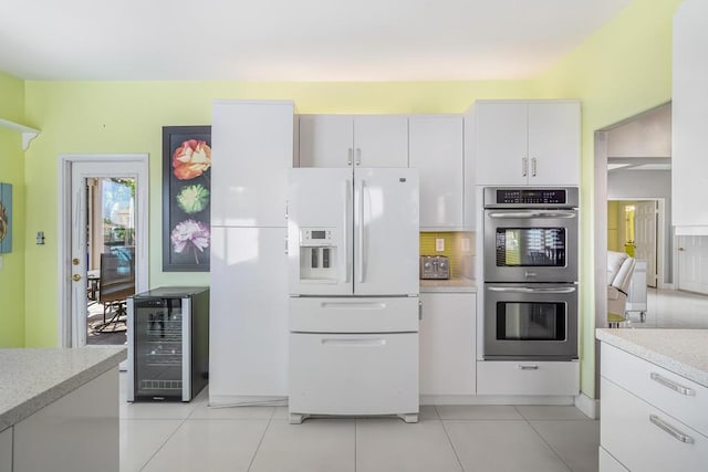 kitchen featuring double oven, beverage cooler, white refrigerator with ice dispenser, light tile patterned floors, and white cabinets