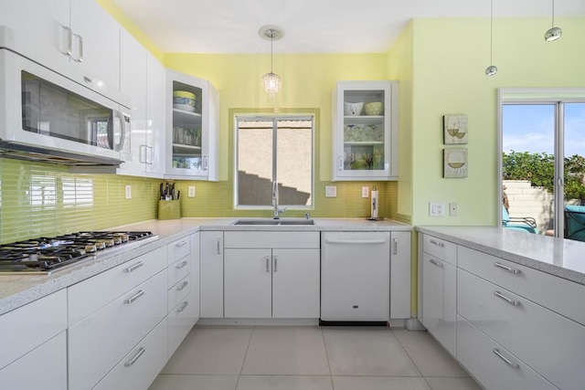 kitchen featuring white appliances, a healthy amount of sunlight, sink, white cabinets, and hanging light fixtures