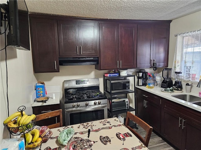 kitchen with a textured ceiling, a sink, stainless steel appliances, light countertops, and under cabinet range hood