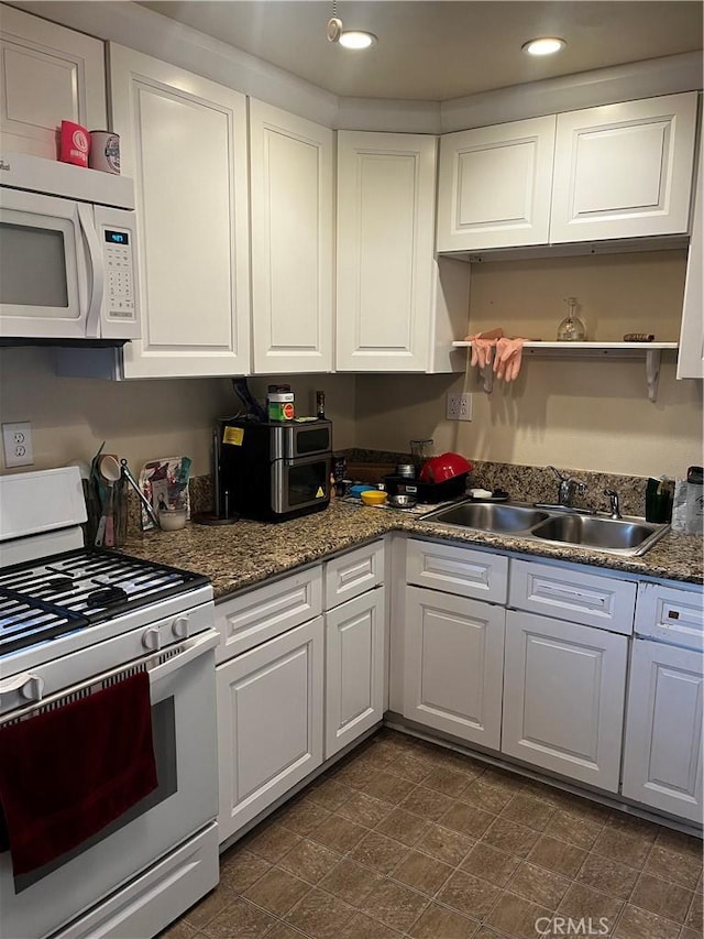 kitchen with white cabinetry, dark stone countertops, white appliances, and sink