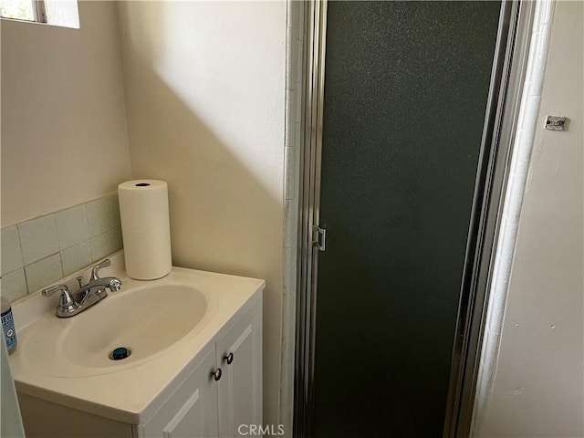 bathroom with backsplash, a shower with door, and vanity