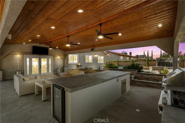 patio terrace at dusk featuring ceiling fan, an outdoor kitchen, wine cooler, and an outdoor hangout area