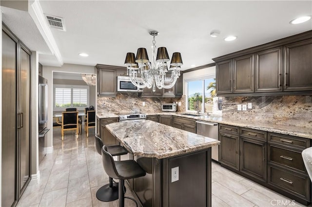 kitchen featuring a center island, light stone countertops, pendant lighting, backsplash, and stainless steel appliances