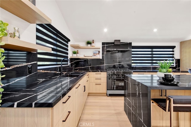 kitchen with light wood-type flooring, backsplash, stainless steel range, sink, and wall chimney range hood