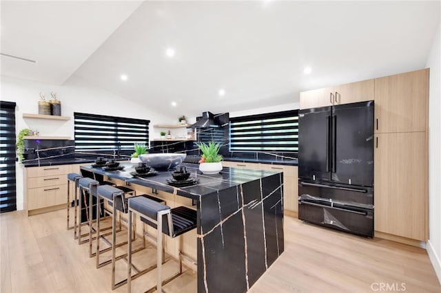 kitchen with lofted ceiling, black refrigerator, light wood-type flooring, light brown cabinetry, and a kitchen island