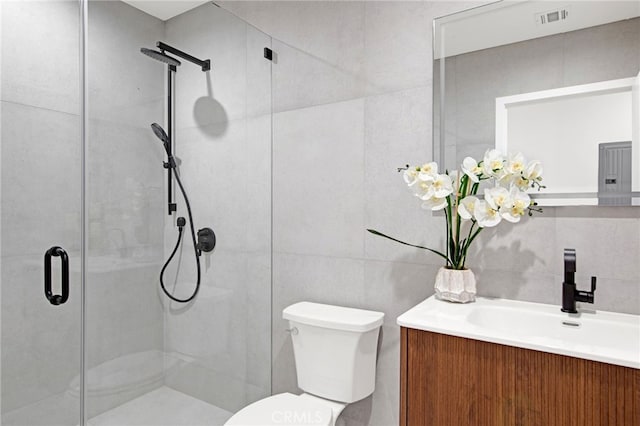 bathroom featuring vanity, toilet, a shower with shower door, and tile walls