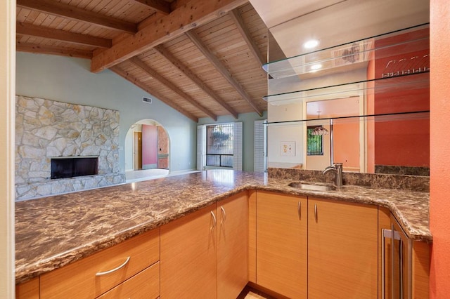 kitchen with wooden ceiling, a stone fireplace, sink, vaulted ceiling with beams, and stone countertops