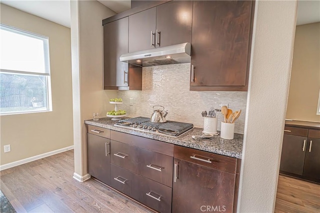 kitchen featuring tasteful backsplash, light stone counters, dark brown cabinetry, light hardwood / wood-style flooring, and stainless steel gas stovetop