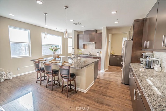 kitchen featuring a breakfast bar area, dark brown cabinets, light stone counters, wood-type flooring, and stainless steel appliances