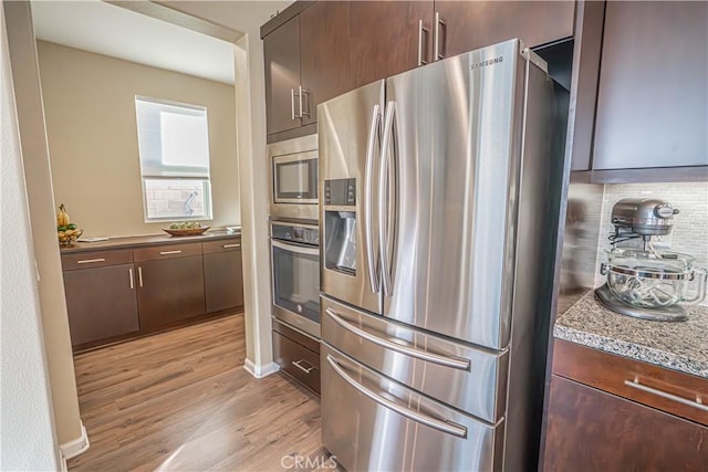 kitchen with dark brown cabinets, light wood-type flooring, stainless steel appliances, and backsplash