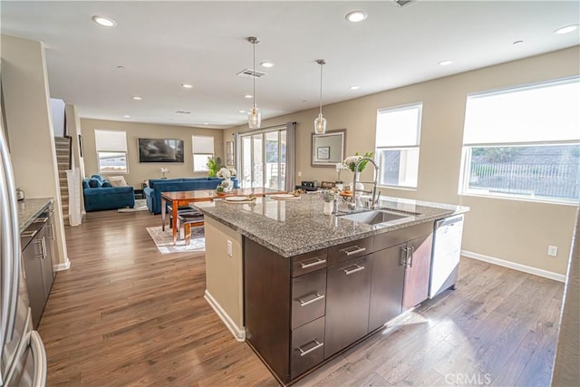 kitchen featuring sink, stainless steel dishwasher, a center island with sink, dark brown cabinets, and hardwood / wood-style flooring