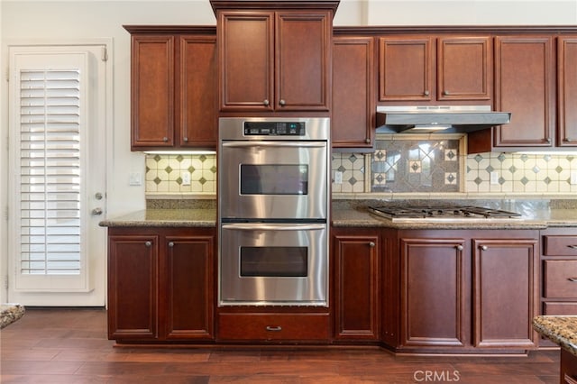 kitchen with decorative backsplash, stainless steel appliances, dark wood-type flooring, and dark stone countertops