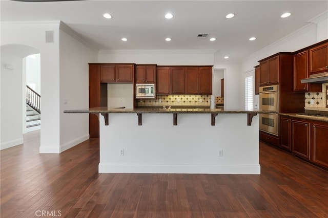 kitchen featuring a kitchen breakfast bar, stainless steel appliances, dark hardwood / wood-style floors, and an island with sink