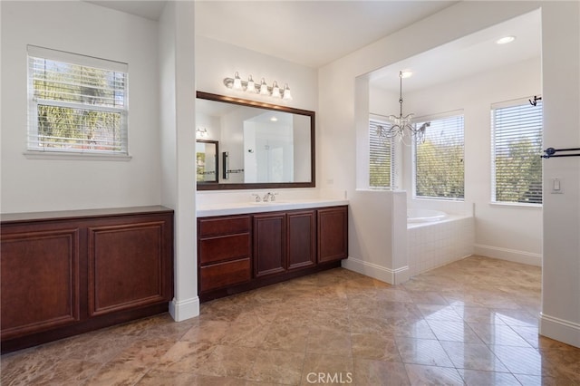 bathroom featuring a notable chandelier, a healthy amount of sunlight, vanity, and tiled bath