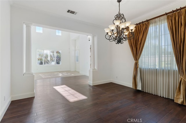 spare room featuring ornate columns, ornamental molding, dark wood-type flooring, and an inviting chandelier