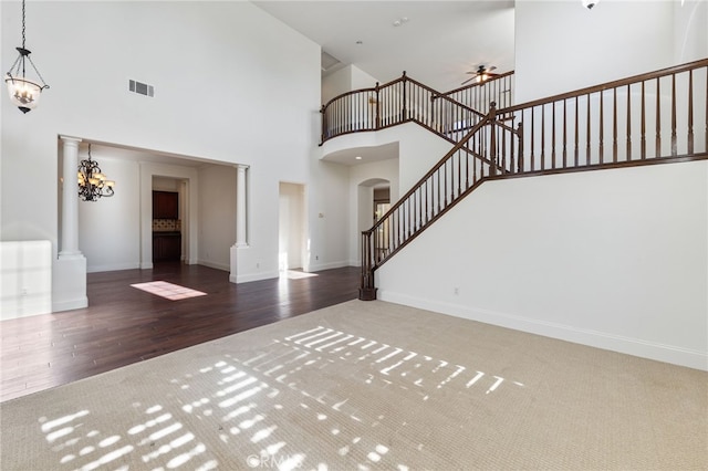 entryway featuring decorative columns, ceiling fan with notable chandelier, dark wood-type flooring, and a high ceiling