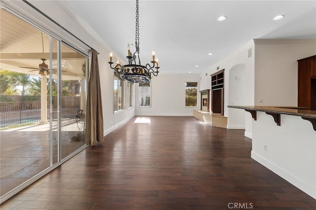 unfurnished dining area featuring ceiling fan with notable chandelier, ornamental molding, and dark wood-type flooring