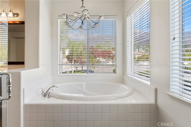 bathroom featuring a notable chandelier and tiled tub