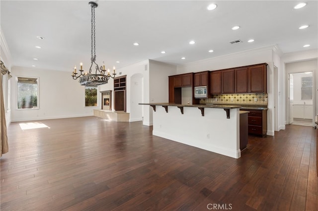 kitchen with pendant lighting, backsplash, dark wood-type flooring, ornamental molding, and a kitchen bar