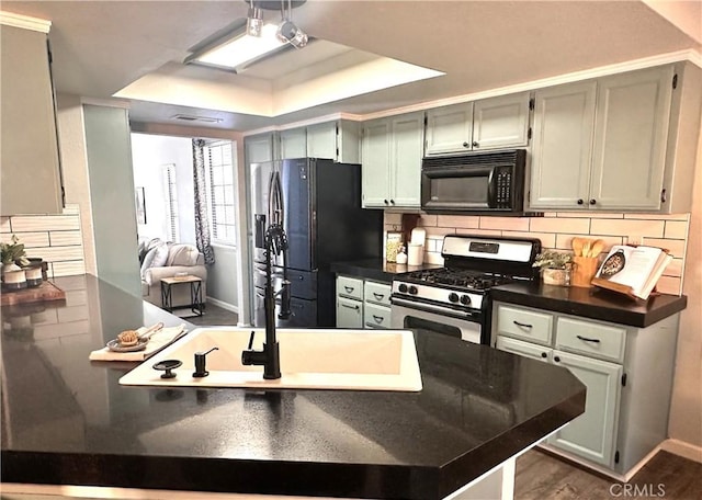 kitchen with black appliances, backsplash, dark hardwood / wood-style floors, kitchen peninsula, and a raised ceiling