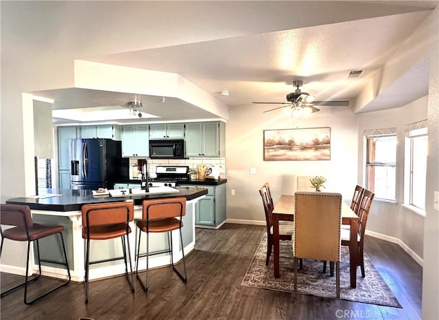 kitchen with kitchen peninsula, green cabinets, appliances with stainless steel finishes, decorative backsplash, and a breakfast bar