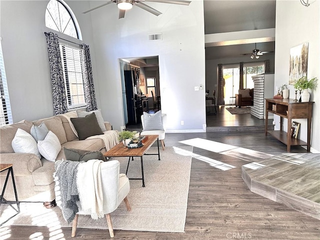 living room with ceiling fan, a towering ceiling, and dark hardwood / wood-style flooring