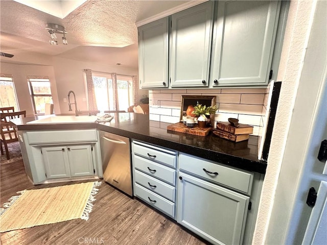 kitchen featuring kitchen peninsula, stainless steel dishwasher, backsplash, and sink