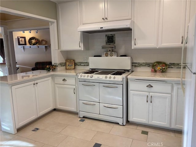 kitchen with kitchen peninsula, backsplash, white appliances, light tile patterned floors, and white cabinetry