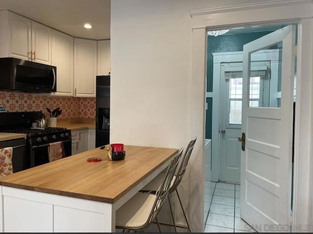 kitchen featuring butcher block countertops, decorative backsplash, white cabinets, and black appliances