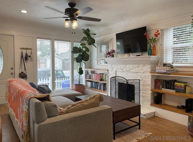 living room featuring hardwood / wood-style floors, ceiling fan, a healthy amount of sunlight, and a stone fireplace