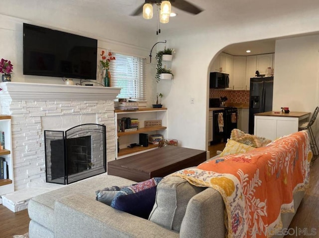 living room with a fireplace, ceiling fan, and dark wood-type flooring