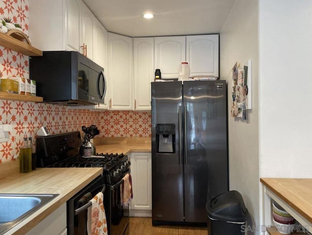 kitchen with white cabinets, light hardwood / wood-style floors, butcher block counters, and black appliances