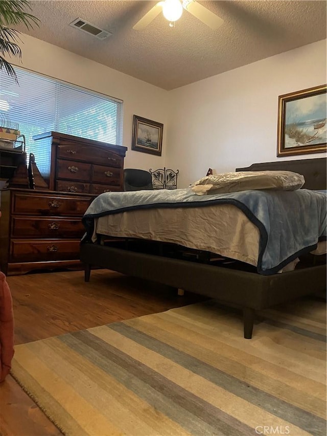 bedroom with ceiling fan, hardwood / wood-style floors, and a textured ceiling