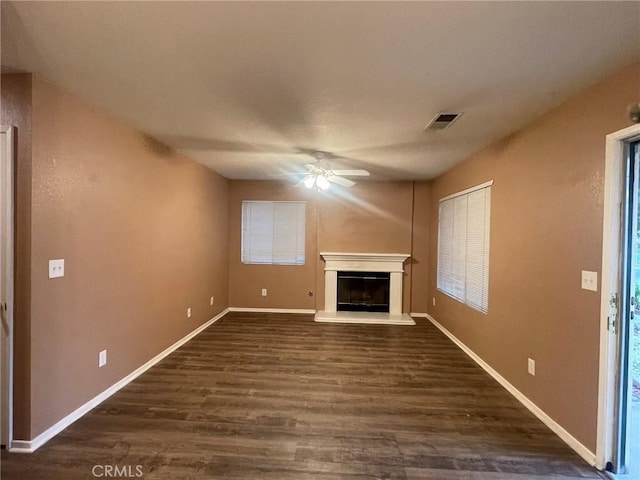 unfurnished living room featuring ceiling fan, a healthy amount of sunlight, and dark hardwood / wood-style flooring