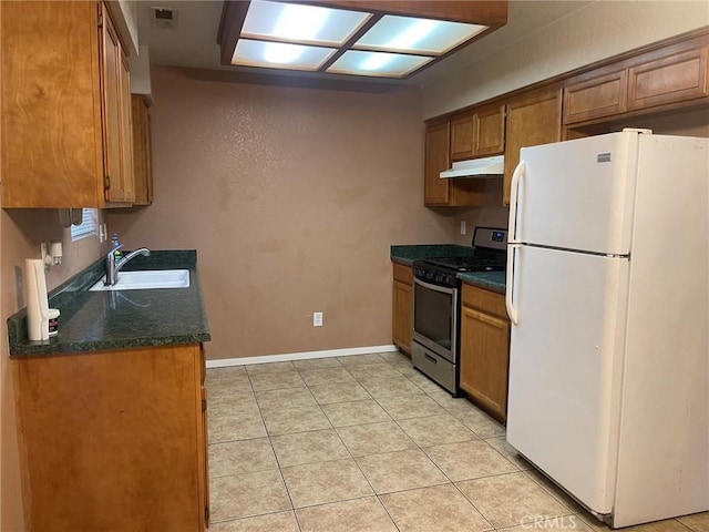 kitchen featuring gas stove, sink, light tile patterned floors, and white refrigerator